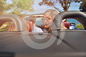 Leisure, road trip, travel and people concept - happy friends driving in cabriolet car along country road