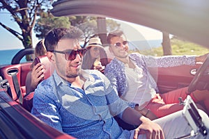 Leisure, road trip, travel and people concept - happy friends driving in cabriolet car along country road