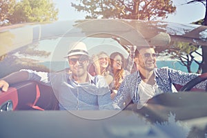 Leisure, road trip, travel and people concept - happy friends driving in cabriolet car along country road