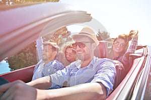 Leisure, road trip, travel and people concept - happy friends driving in cabriolet car along country road