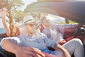 Leisure, road trip, travel and people concept - happy friends driving in cabriolet car along country road