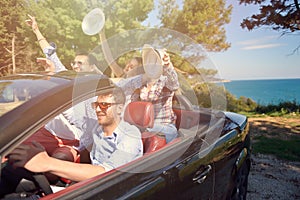 Leisure, road trip, travel and people concept - happy friends driving in cabriolet car along country road