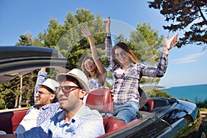 Leisure, road trip, travel and people concept - happy friends driving in cabriolet car along country road