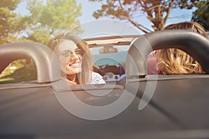 Leisure, road trip, travel and people concept - happy friends driving in cabriolet car along country road