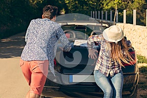 Leisure, road trip, travel and people concept - happy friends pushing broken cabriolet car along country road