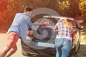 Leisure, road trip, travel and people concept - happy friends pushing broken cabriolet car along country road