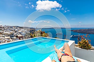 Leisure summer vacation. Infinity pool model in bikini on the sun-tanned slim legs over caldera in Santorini Greece