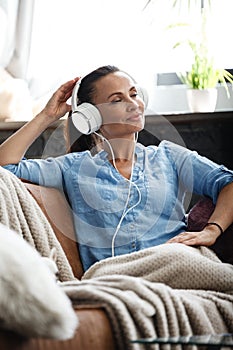 Leisure time concept. Happy beautiful woman listening to the music using headphones sitting on a couch indoors. Female