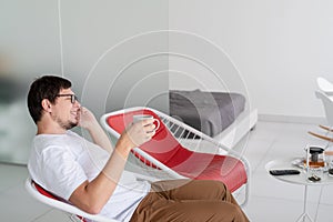 Man sitting in a chair watching tv holding tea cup and phone