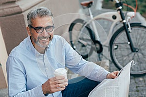 Leisure time in town. man reading newspaper and having cup of coffee, blurred bicycle in background