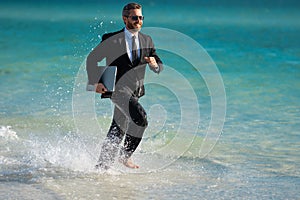 Leisure weekend and remote freelance work. Crazy comic business man in suit run on sea. Funny businessman with laptop