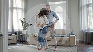 Leisure Young Family Dad And Mom Dance In The Room Barefoot And Young Son Jumps On The Couch.