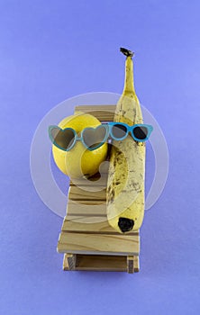 Lemon and banana with sunglasses resting on the wooden beach bed. Summer vacation concept on purple background