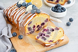 Lemon blueberry cake with lemon icing and fresh berries on top on the board on a gray concrete background with cup of tea.