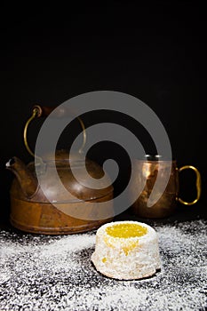 Lemon cake with powdered sugar on dark background with copper tea pot and mug