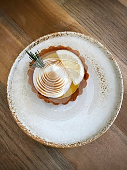 Lemon cheese tart with white ceramic plate on wooden table and chair in minimal coffee cafe.