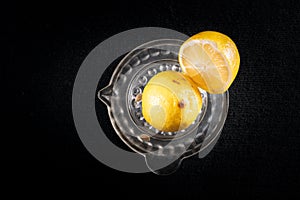 Lemon cut in half, on a glass lemon squeezer. Black background