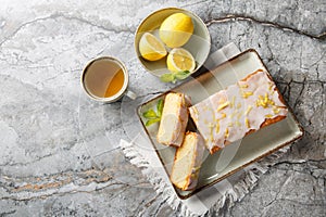 Lemon drizzle cake with lemon zest and icing is a classic British tea-time treat closeup on the plate. Horizontal top view