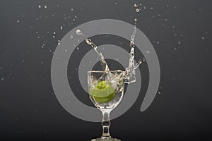 Lemon falling into a glass of transparent water causing splashes upwards. Isolated on gray background