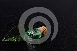 Lemon flavor of emerald color in a glass bottle with a wooden stopper on a green leaf with water droplets