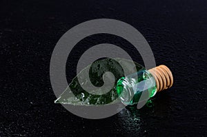 Lemon flavor of emerald color in a glass bottle with a wooden stopper on a green leaf with water droplets