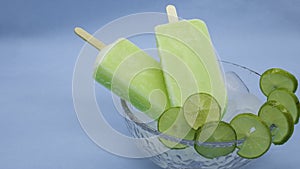 Lemon flavor ice pops, inside a deep plate with ice on a blue background, with lemon slices on the plate