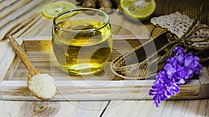 Lemon honey tea mixed with ginger in a clear glass, with a spoon and  brown sugar and hemp bag placed in a wooden tray on a brown