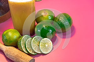 Lemon juice and lemonade Citrus aurantifolia amid wooden pestle and fresh fruits on pink background