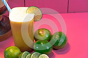 Lemon juice and lemonade Citrus aurantifolia amid wooden pestle and fresh fruits on pink background