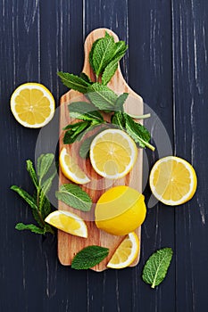 Lemon and mint leaves served on wooden kitchen board on black rustic table, ingredient for summer cocktails and lemonade