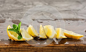 Lemon and mint leaves served on wooden kitchen board on concrete table, ingredient for summer cocktails and lemonade