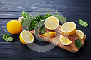 Lemon and mint served on wooden kitchen board on black rustic table, ingredient for summer cocktails and lemonade