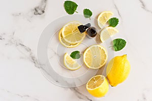 Lemon oil in a bottle with a ppetka with green melisa leaves and lemon slices on a white marble background. top view. moisturizing photo