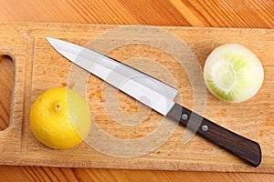 Lemon, onion and kitchen knife on a wooden board