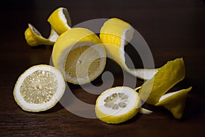 Lemon peel or lemon twist on a dark brown wooden background. Lemon slices are cut across. Close up.