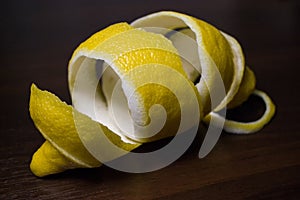 Lemon peel or lemon twist on a dark brown wooden background. Lemon slices are cut across. Close up.