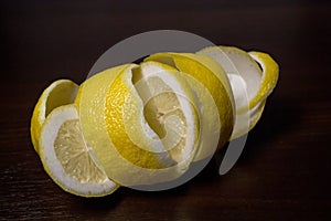 Lemon peel or lemon twist on a dark brown wooden background. Lemon slices are cut across. Close up. Citrus limon