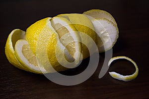 Lemon peel or lemon twist on a dark brown wooden background. Lemon slices are cut across. Close up. Citrus limon