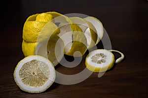 Lemon peel or lemon twist on a dark brown wooden background. Lemon slices are cut across. Close up.