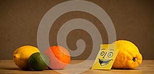 Lemon with post-it note smiling at citrus fruits