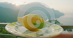 Lemon rests on a plate with the sun rising over the sea. Morning's early light gently kisses the citrus on a balcony