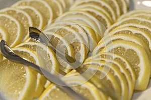 Lemon slices with metal tongs on a plate on the buffet table. Close-up.