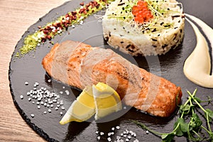 Lemon slices red fish rice and caviar on a black round wooden tray