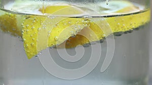 Lemon in sparkling water in a glass on a table in the sun, water with lemon