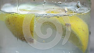 Lemon in sparkling water in a glass on a table in the sun, water with lemon