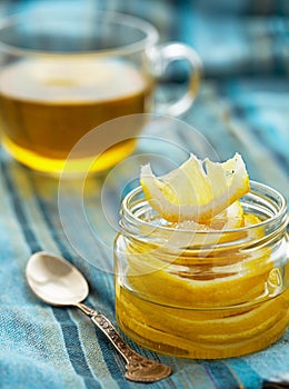 Lemon with sugar is in a glass jar, next is a cup of tea