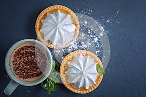 Lemon tart with mint leaves and a cup of cappuccino with chocolate topping