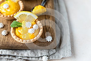 Lemon tartlets. Homemade shortbread mini tarts with lemon curd and meringue on wooden board, light background