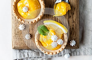 Lemon tartlets. Homemade shortbread mini tarts with lemon curd and meringue on wooden board, light concrete background. Top view