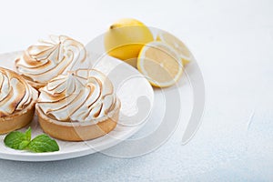 Lemon tartlets with meringue on vintage white plate on the stone table. Tasty treat on a light blue background. With copy space